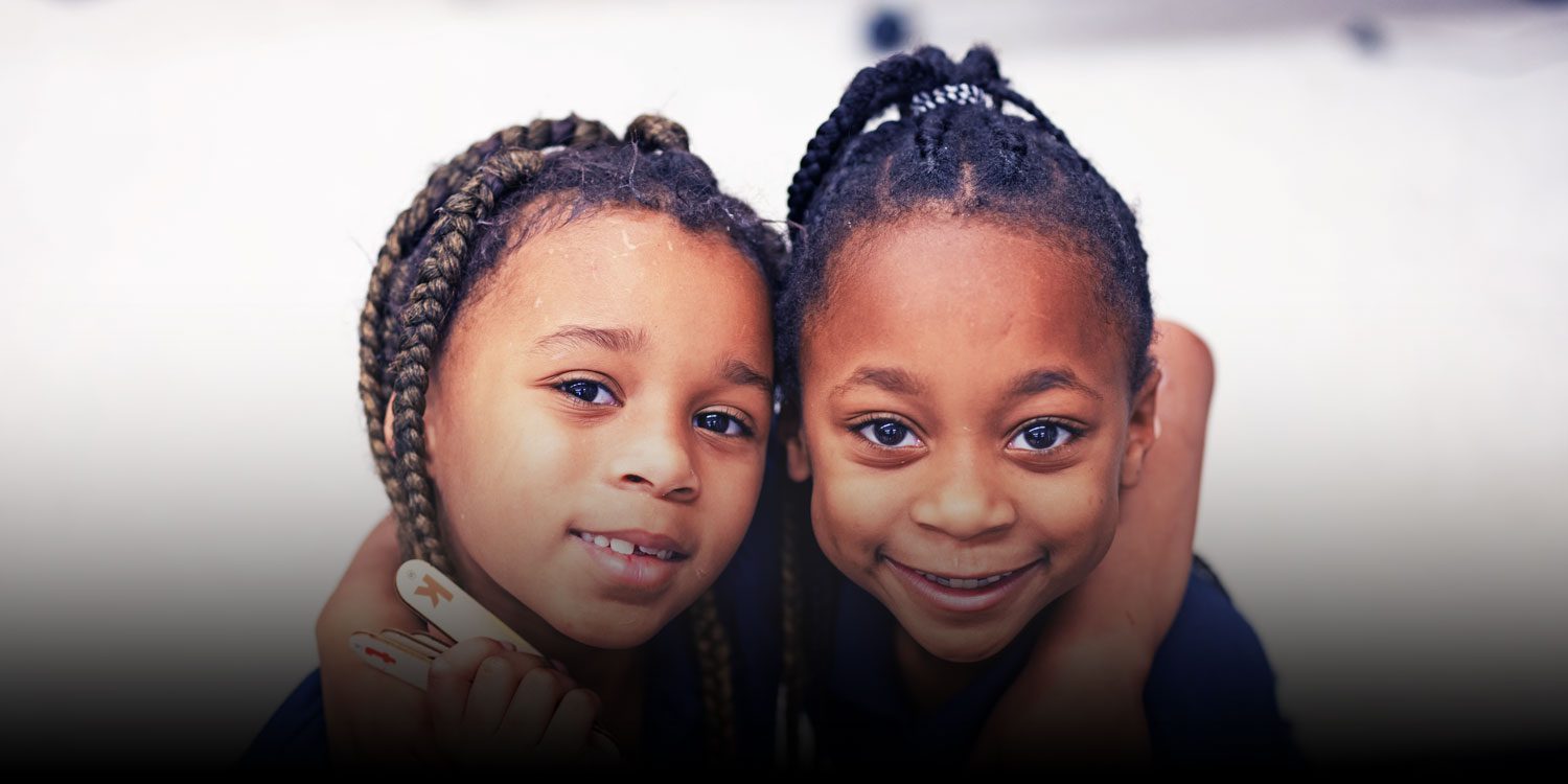 Two smiling students with their arms around each other in class.